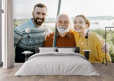 Portrait of a young man and woman with cheerful senior grandfather hugging together outdoors, having a good time while fishing Wall mural