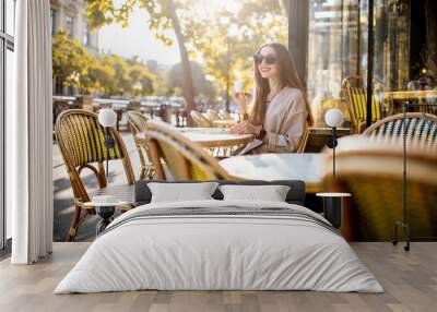 Portrait of a young woman enjoying coffee sitting outdoors at the traditional french cafe during the morning in Paris Wall mural