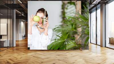 Portrait of a young woman with apple and smoothie drink indoors. Healthy eating and wight loss concept Wall mural