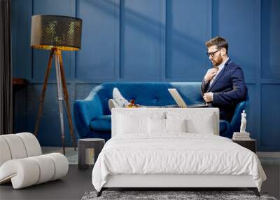 Portrait of an elegant businessman sitting with laptop on the couch at the luxury blue office interior Wall mural