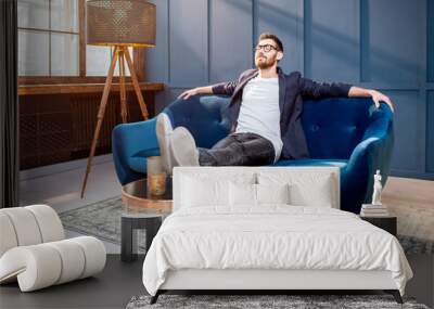 Portrait of relaxed businessman dressed casualy sitting on the couch at the luxury office with blue walls Wall mural