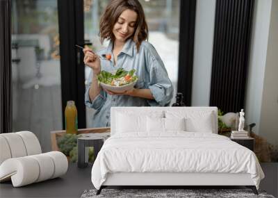 Portrait of young woman smiling and eating healthy green salad with tomato at home. Health care and wellness concept. High quality photo Wall mural