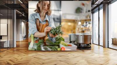 Pretty woman with green ingredients and spicy herbs cooking healthy food on the kitchen. Healthy and wellness concept. High quality photo Wall mural