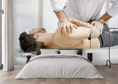 Professional senior physiotherapist doing manual treatment to a man in the cabinet of rehabilitation clinic Wall mural