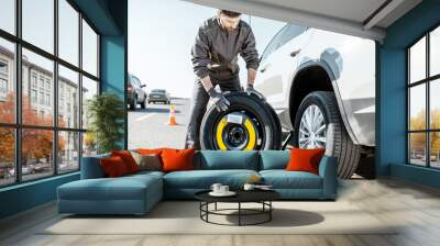 Road assistance worker in uniform changing car wheel on the highway Wall mural