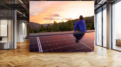 Rooftop with solar panels on house in mountains, woman sitting alone enjoying sunset. Energy independence, sustainability, self sufficient, and escapism to nature concept Wall mural