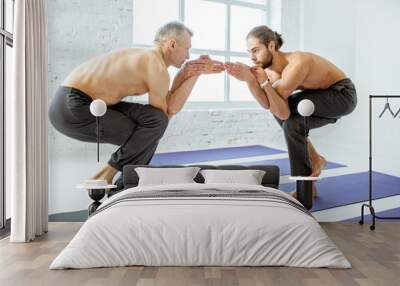 Senior and young man with naked torso practising yoga poses together in the white studio Wall mural