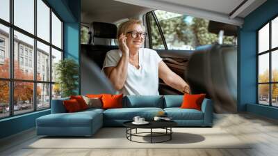 Senior business woman talking with phone while sitting on the back seat in the modern car. Concept of a business life on retirement Wall mural