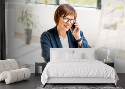 Senior businesswoman working with laptop and talking phone at the bright modern office interior Wall mural