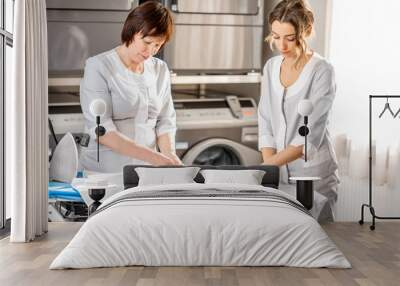 Senior washwoman and young assistant ironing white shirt with professional iron in the laundry Wall mural