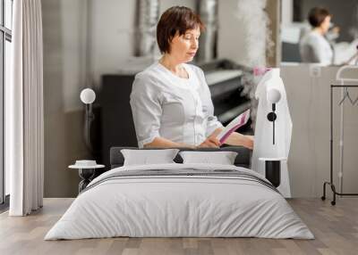 Senior washwoman in uniform ironing up a white shirt with vapor machine in the professional laundry Wall mural