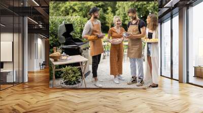 Small group of young friends have fun while cooking food on grill at backyard on nature. Eating and spending summertime together outdoors Wall mural