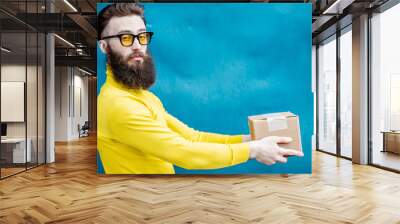 Stylish bearded man in yellow sweater standing with gift box on the blue background Wall mural