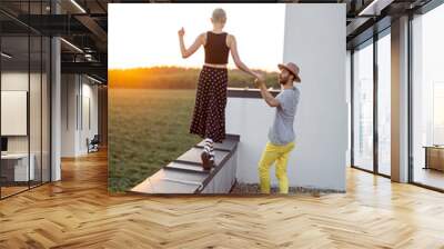 Stylish girl walks along the parapet of the roof with her boyfriend at sunset. Carefree lifestyle and romance concept Wall mural