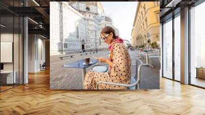 Stylish woman sitting with phone on cafe terrace near famous Duomo cathedral in Florence during morning time. Concept of italian lifestyle and travel Italy Wall mural