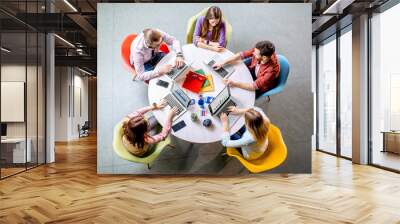 Team of a young coworkers dressed casually working together with laptops sitting at the round table in the office, view from above Wall mural