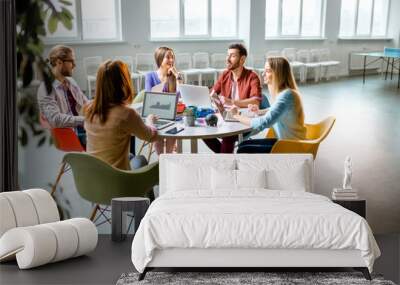 Team of a young coworkers dressed casually working together with laptops sitting at the round table in the office Wall mural