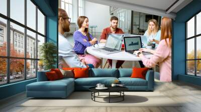 Team of a young coworkers dressed casually working together with laptops sitting at the round table in the office Wall mural