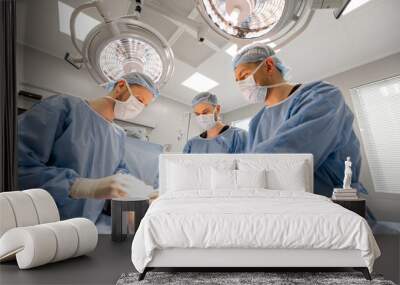 Three confident surgeons performing surgical operation on a patient's knee in operating room. Concept of real surgery and invasive treatments Wall mural