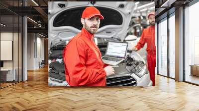 Two auto mechanics in red uniform doing engine diagnostics with computer in the car service Wall mural