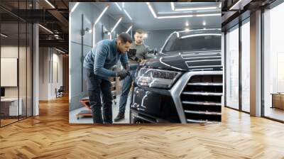 Two car service workers examining vehicle body for scratches and damages while taking a car for professional automotive detailing Wall mural