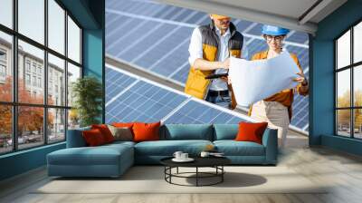 Two engineers or architects examining the construction of a solar power plant, standing with blueprints between rows of solar panels Wall mural