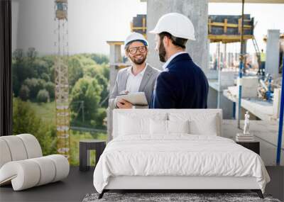 Two engineers or architects supervising the process of residential building construction standing on the structure outdoors Wall mural