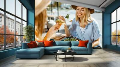 Two female best friends eating healthy food while sitting together on a restaurant terrace on a summer day Wall mural