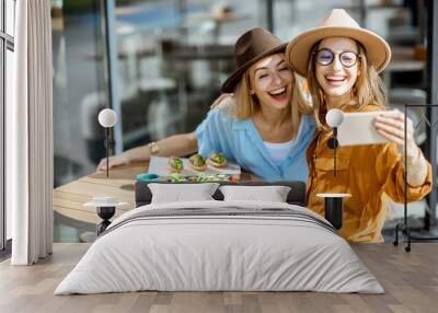 Two female best friends making selfie photo while sitting together on a restaurant terrace and eating healthy food Wall mural