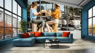 Two female best friends spending time together sitting with a gift on the terrace in a cafe, having fun during a summer day Wall mural