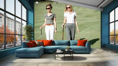 Two female best friends walking with golf equipment on beautiful playing course, talking and having fun during a game on a sunny day Wall mural