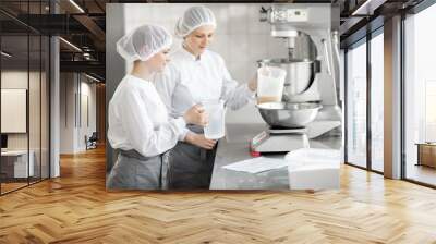 Two female confectioners in uniform weighing ingredients for pastry working at the bakery manufacturing Wall mural