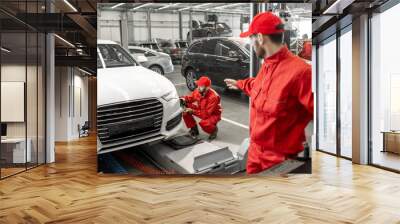 Two handsome auto mechanics in red uniform making wheel alignment with professional tools and computer at the car service Wall mural