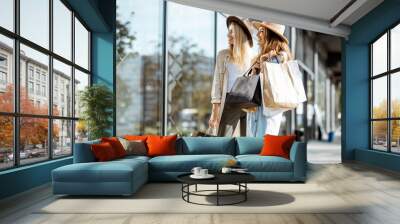 Two happy girlfriends looking on the shopwindow while standing with shopping bags near the mall Wall mural