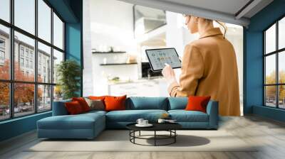 Woman controlling smart home devices using a digital tablet with launched application in the white living room. Smart home concept Wall mural