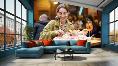 Woman eating italian meat appetizer, various sliced meat and cheese with bread and Aperol Spritz at bar or restaurant outdoors. Concept of Italian lifestyle and gastronomy Wall mural