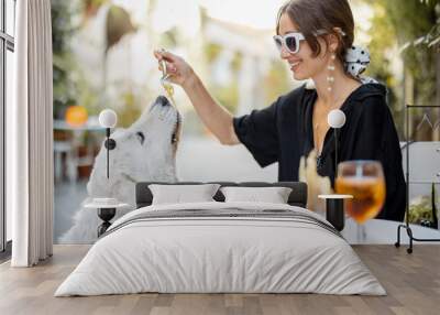 Woman eating pasta with her cute white dog at the restaurant outdoors. Concept of friendship with pets and having fun together Wall mural