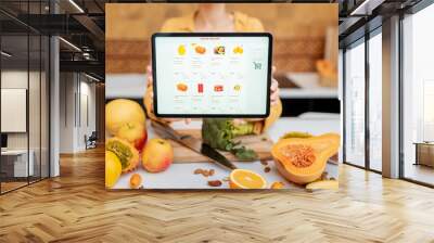 Woman holding digital tablet with launched online shopping market while standing on the kitchen with lots of fresh food on the table Wall mural