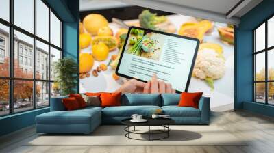 Woman looking on the digital recipe, using touchscreen tablet while cooking healthy meal on the kitchen at home, close-up view on the screen Wall mural