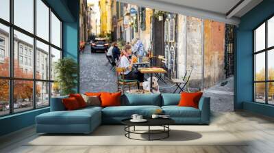 Woman sitting at traditional restaurant on the beautiful cozy street in Rome. Concept of Italian gastronomy and travel. wide street view Wall mural