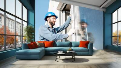 Workman in uniform mounting windows checking the level on the white building facade Wall mural