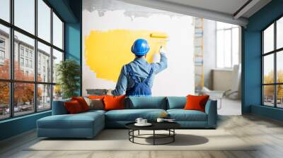 Workman in uniform painting wall with yellow paint at the construction site indoors Wall mural