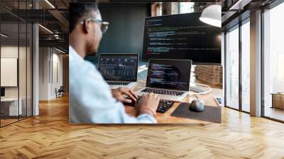 young african male programmer writing program code sitting at the workplace with three monitors in t Wall mural