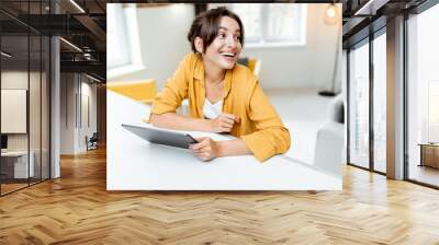 Young and cheerful woman using a digital tablet while sitting relaxed at home. Concept of a leisure activities with mobile devices at home Wall mural