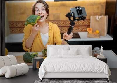 Young and cheerful woman vlogging on mobile phone about healthy food and cooking. Concept of healthy eating and social media influencing Wall mural