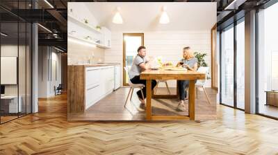 Young and happy couple having a breakfast sitting at the wooden table of the dining room of the modern country house. Wide angle view Wall mural