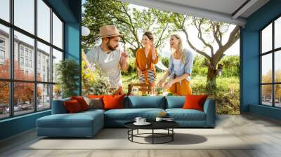 Young and happy friends serving table with food, preparing for the festive lunch in the beautiful garden during the sunny weather Wall mural