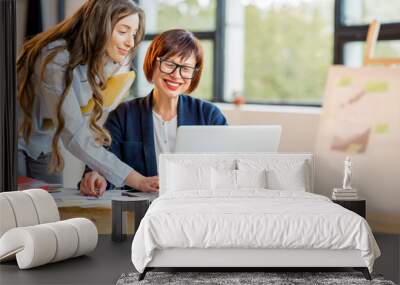 Young and older businesswomen working together on documents at the modern office interior Wall mural