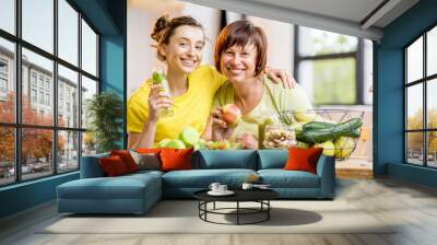 Young and older women sitting with healthy food and fresh drinks after the sports training indoors on the window background Wall mural