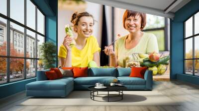 Young and older women sitting with healthy food and fresh drinks after the sports training indoors on the window background Wall mural